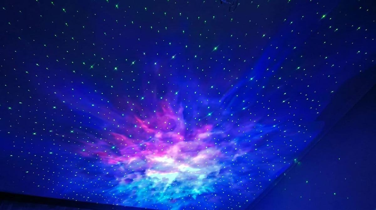 Galaxy projector casting a blue, purple and teal nebula with green stars across a bedroom ceiling